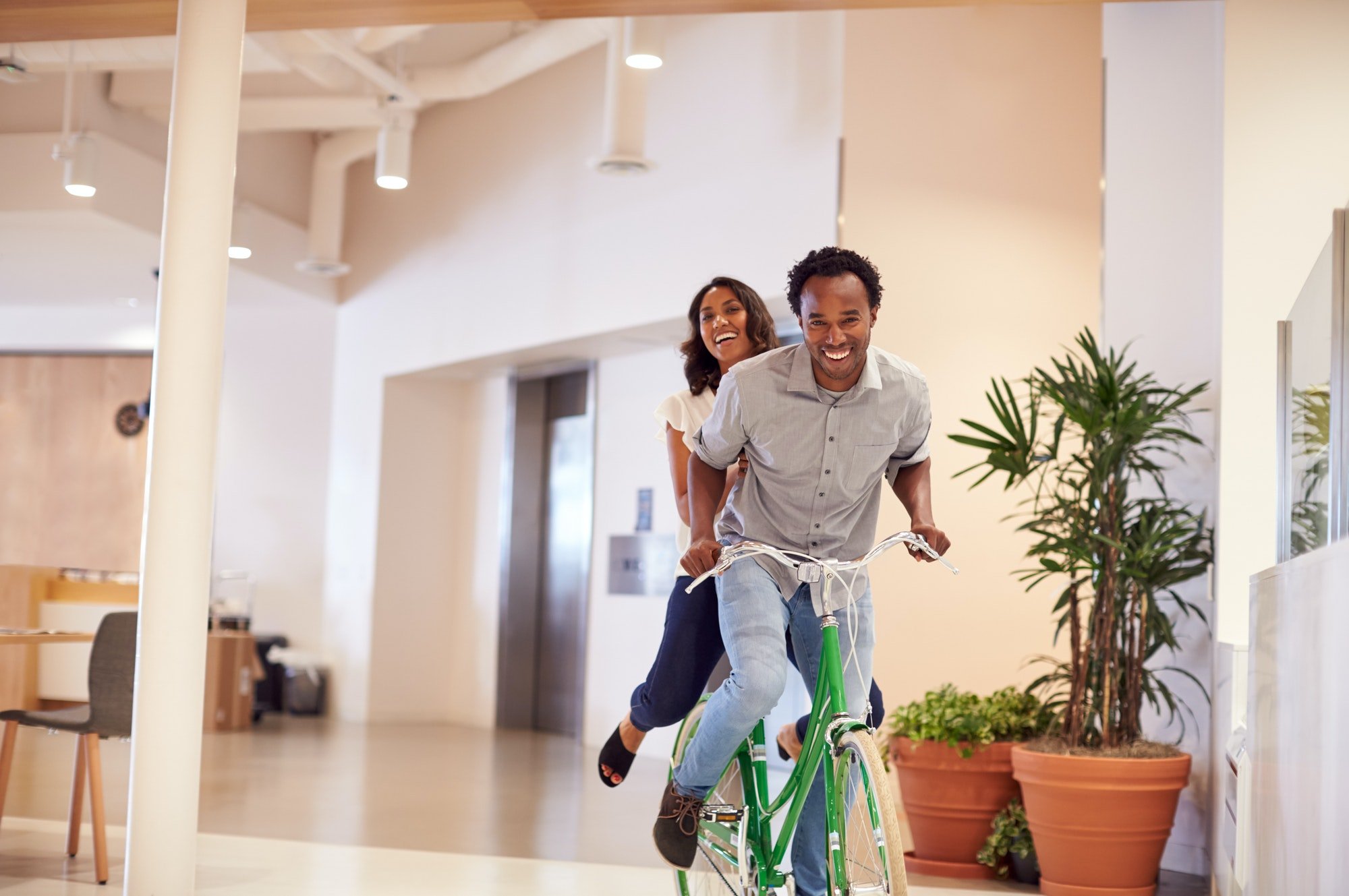 Businessman And Businesswoman Having Fun Riding Bike In Office After Cycling To Work